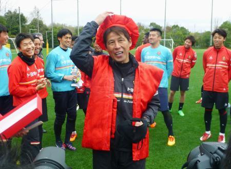 　６０歳の誕生日に、赤いちゃんちゃんこと頭巾を贈られて喜ぶＪ１名古屋の西野監督（中央）＝７日、愛知県豊田市のトヨタスポーツセンター