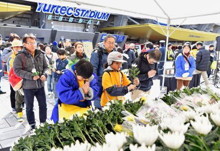 　東日本大震災から６年を迎え、ユアテックスタジアム仙台に設置された献花台で手を合わせる人たち＝１１日午後、仙台市