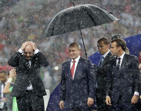 　１５日、モスクワのルジニキ競技場で行われた決勝戦後、頭に手をやるインファンティノＦＩＦＡ会長（左）と傘の下に立つロシアのプーチン大統領（中央）、それを見るフランスのマクロン大統領（右）（ＡＰ＝共同）