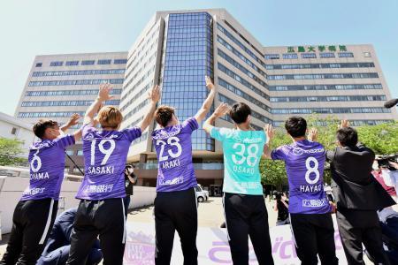 　広島大学病院を訪問し、病棟に向かって手を振るサッカーＪ１広島の選手ら＝１３日午後、広島市