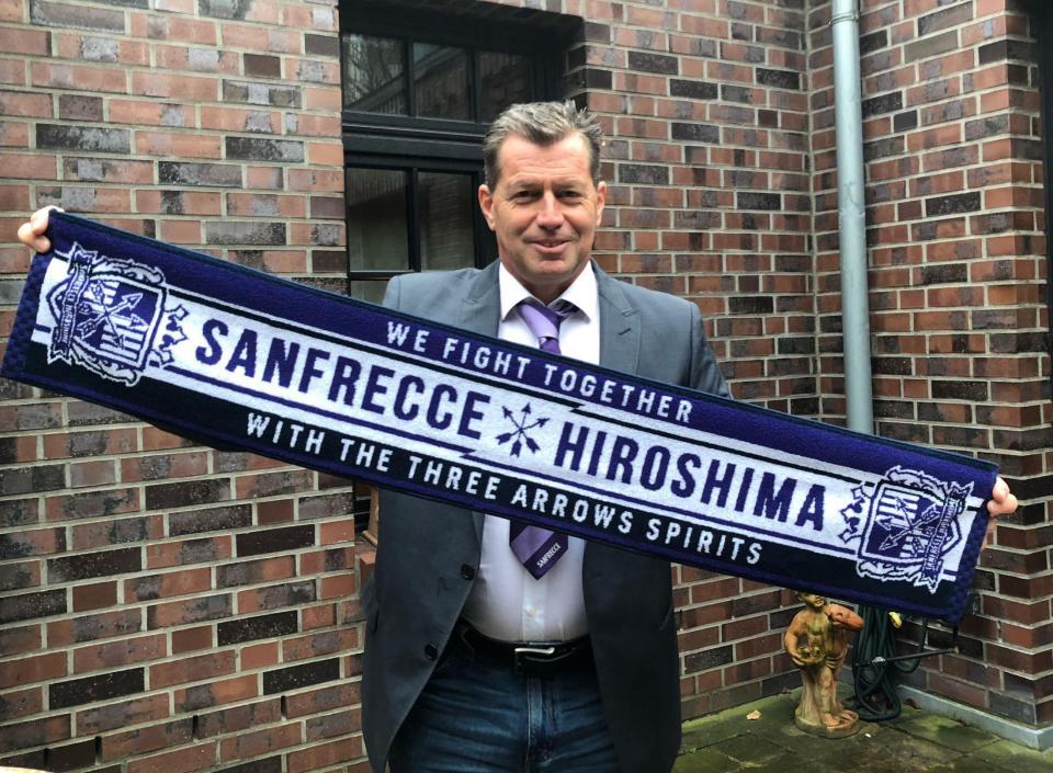 サンフレッチェのマフラータオルを手にするスキッベ新監督（（Ｃ）２０２１Ｓ．ＦＣ）
