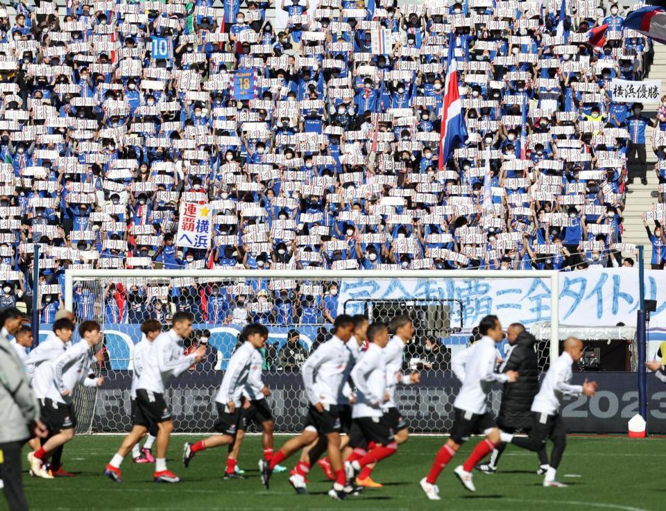 　皆でボードを掲げて横浜Ｍイレブン（手前）を鼓舞する横浜Ｍサポーター（撮影・吉澤敬太）