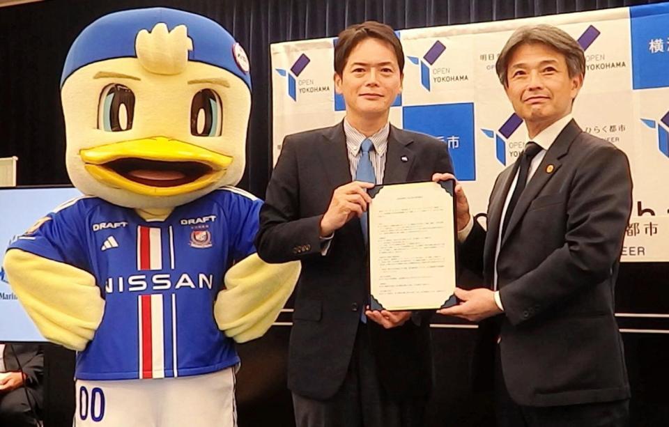 　マスコットのマリノスケも駆けつける中で協定書を掲げる横浜Ｍの中山社長（右）と山中横浜市長