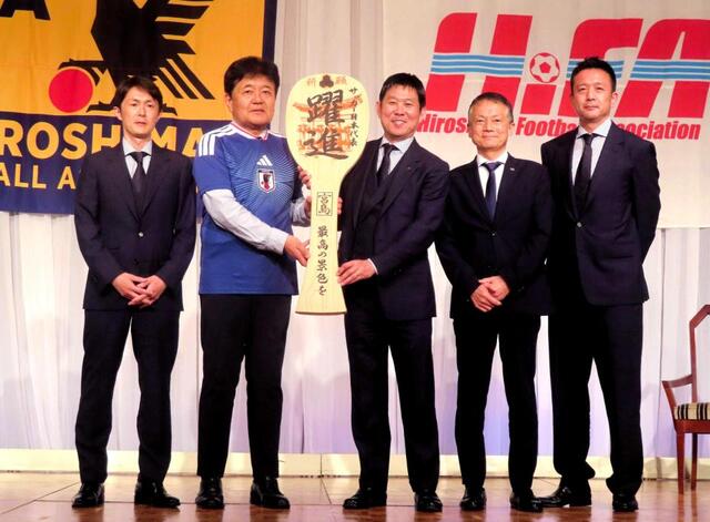 広島県サッカー協会の宗政潤一郎会長（左から２人目）から記念品の巨大しゃもじを受け取ったサッカー日本代表の森保一監督（中央）。左端から中下征樹テクニカルスタッフ、（２人空けて）湯川和之ＪＦＡ専務理事、下田崇ＧＫコーチ（撮影・松田和城）