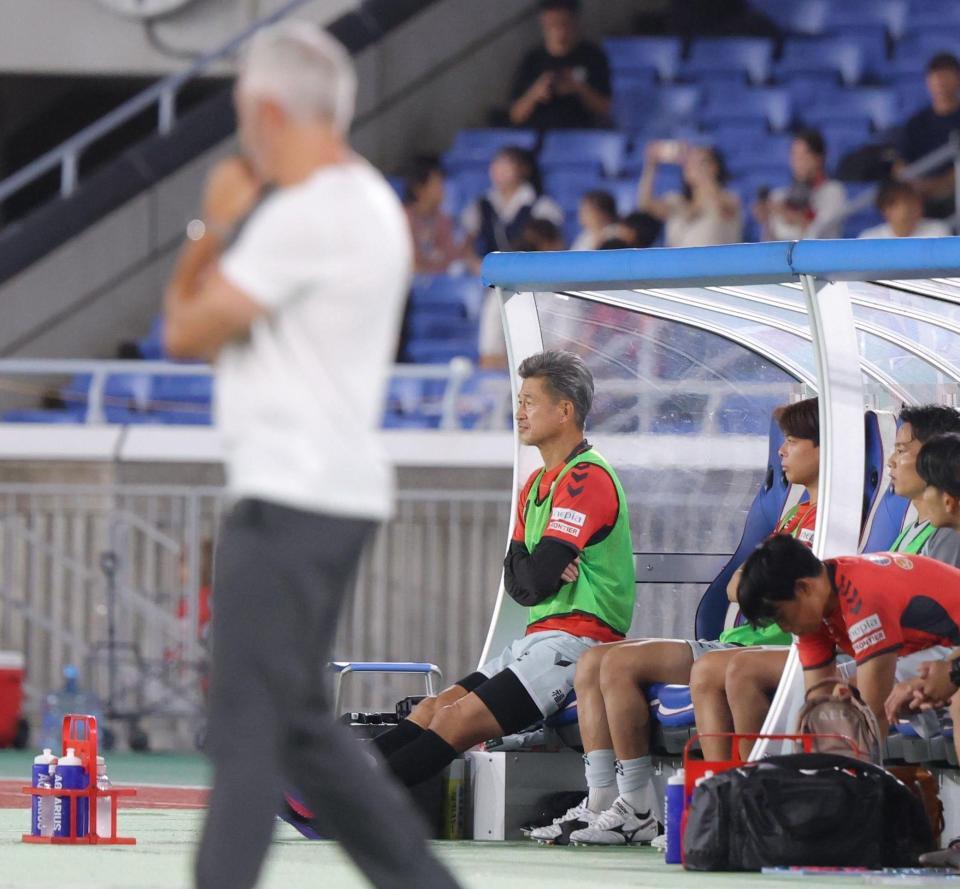 前半、ベンチから試合を見つめる福島・三浦知良。手前は横浜Ｍのスティーブ・コリカ監督（撮影・吉澤敬太）