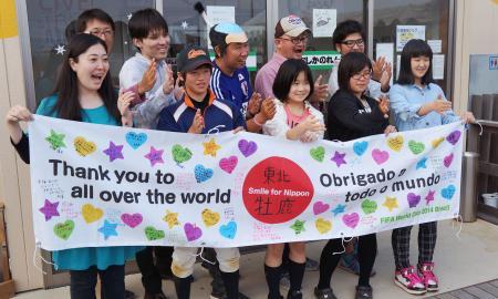 　スタジアムに掲げる予定の横断幕を広げる角田寛和さん（後列中央）と宮城県石巻市の牡鹿中の生徒（前列右の４人）＝５月、石巻市（角田さん提供）