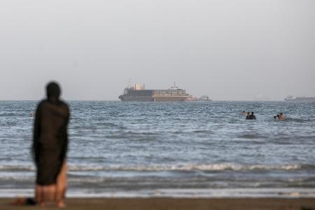 　ホルムズ海峡通過の許可を待つ貨物船と、ペルシャ湾沿岸に見える人々＝１５日、イラン・バンダルアバス（ゲッティ＝共同）