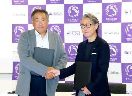　ソフトバンクの常務執行役員（左）と握手する東北大の越村俊一教授＝２７日午後、東京都港区