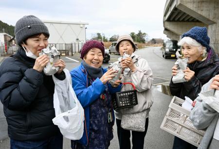 　石川県珠洲市の仮設住宅で振る舞われた焼き芋を笑顔で食べる女性＝２９日午前