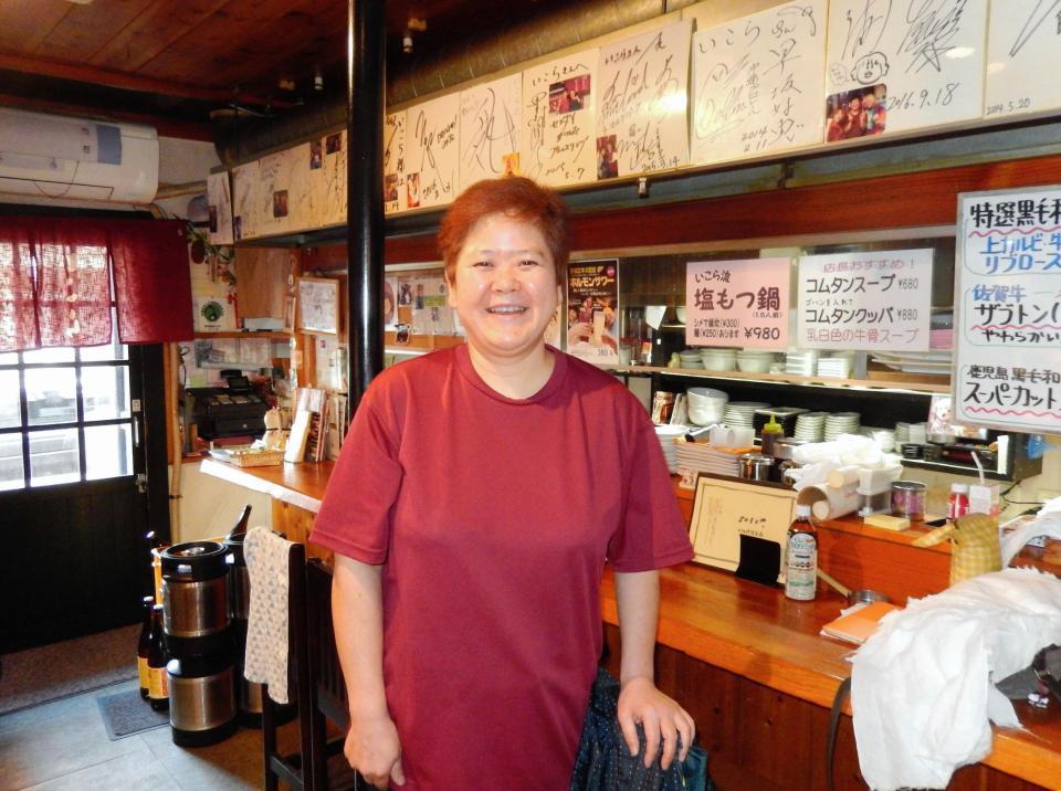 レスラー仲間のサインが飾られた店内で笑顔を見せる豊田記代さん