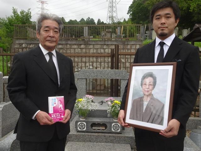 井手久美子さんの墓前で、著書を手にする長男・純さん(左)と孫の悠介さん＝千葉・君津市の圓明院