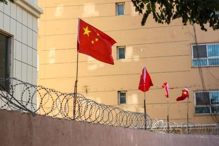新疆ウイグル自治区・カシュガルの有刺鉄線の壁にある中国の旗（Jonathan Densford/stock.adobe.com）