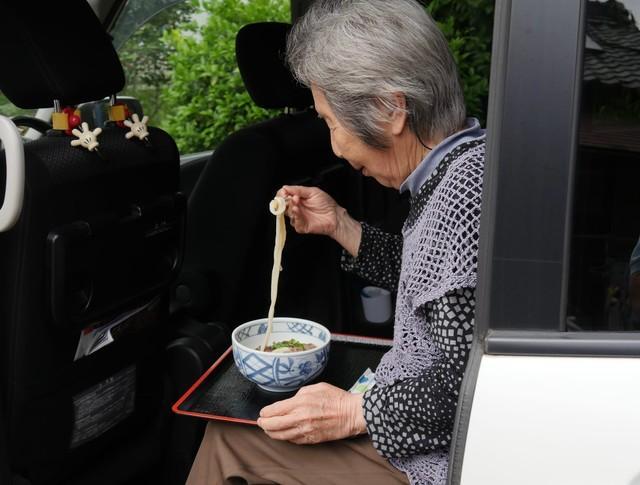 後部座席でうどんを食べるおばあちゃん　※再現写真（松浦産業提供）