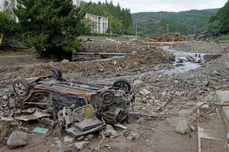 　記録的豪雨で氾濫した塚田川沿いで、ひっくり返ったまま残る車＝２０日午前、石川県輪島市久手川町