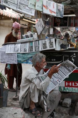 　パキスタンの首都イスラマバードで、米イランの戦闘終結に向けた覚書を巡るニュースを読む男性＝１４日（ロイター＝共同）