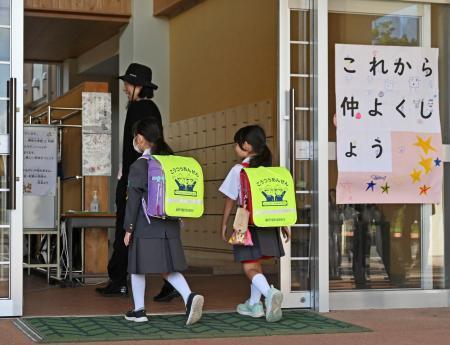 　「これから仲よくしよう」のボードが掲げられた石川県能登町立柳田小に入る輪島市立町野小の児童ら＝１日午前、能登町