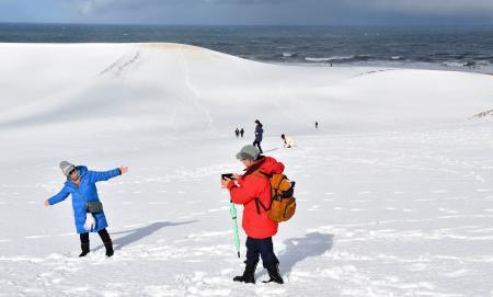 　強い冬型の気圧配置が続き、一面が雪に覆われた鳥取砂丘で記念撮影する観光客。ねずみ色の雲の隙間から日差しが降り注ぎ、白銀の世界が広がった＝１０日午前、鳥取市