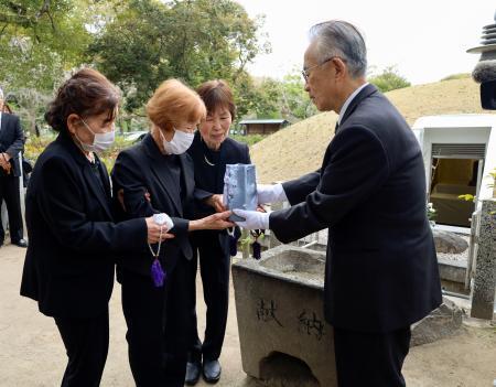 　１３歳で被爆して亡くなった梶山初枝さんの遺骨を受け取る妹の美智子さん（左から２人目）。右奥は原爆供養塔＝２２日午前、広島市の平和記念公園