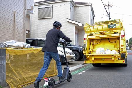 　実証実験で、ごみの集積場所の間を電動キックボードで移動する作業員＝２１日午前、相模原市