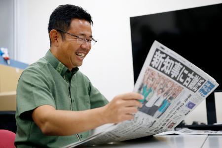 　沖縄県知事選から一夜明け、当選を伝える新聞を手にする古謝玄太氏＝１４日午前、那覇市