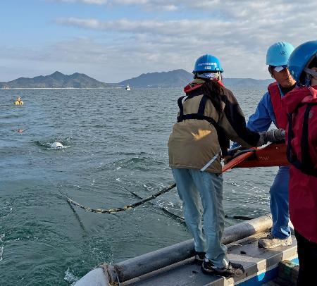 　愛媛県上島町の沖合で、海面に探査装置を延ばす産総研の研究員ら＝２０２５年１１月（産総研提供）