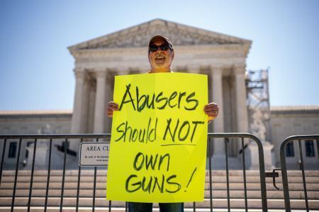 　２１日、米ワシントンの最高裁判所前で「虐待者は銃を持つべきではない」と書かれたプラカードを掲げる男性（ゲッティ＝共同）