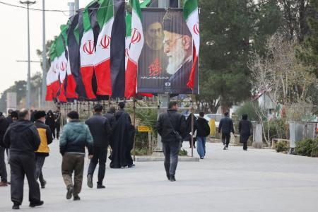 　９日、イラン・テヘランで、国旗や殺害されたハメネイ師のポスターが掲げられた通りを歩く人（ＷＡＮＡ提供・ロイター＝共同）