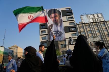 　イランの最高指導者モジタバ・ハメネイ師の肖像の前で国旗を持つ女性＝４日、テヘラン（ＡＰ＝共同）