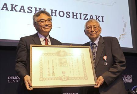 　２３日、室田幸靖駐ロサンゼルス総領事（左）から勲記を手渡されたタカシ・ホシザキさん＝米ロサンゼルス（共同）
