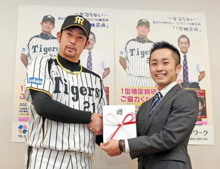 　日本ＩＤＤＭネットワークの大村専務理事（右）に寄付金を手渡し、握手を交わす岩田