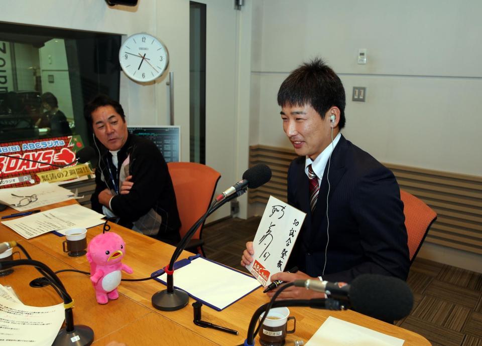 阪神・岩崎優はラジオに出演し来季の目標「５０試合登板」と色紙に書く（左は中西清起氏）＝朝日放送（撮影・山口登）