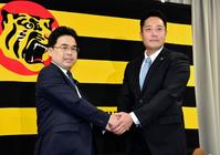 阪神２軍育成コーチ就任が決まり谷本修球団本部長（左）とがっちり握手を交わす阪神の日高剛＝球団事務所（撮影・持木克友）