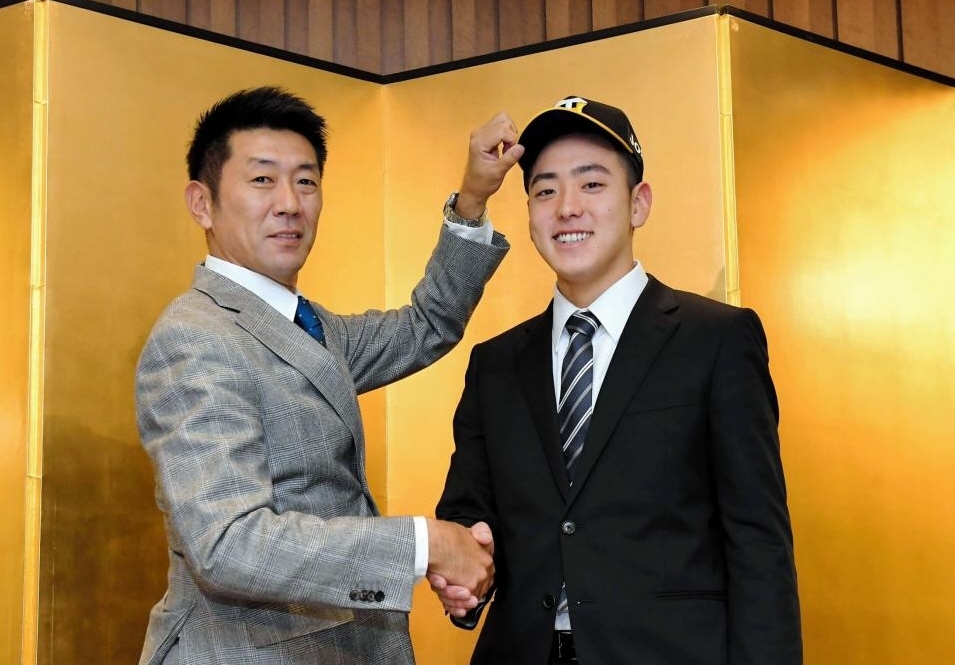 仮契約を交わし、阪神・田中スカウト（左）に帽子を被せてもらう東海大九州・小川一平＝熊本市内のホテル（撮影・高部洋祐）