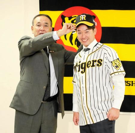 木戸プロスカウト部長（左）から帽子をかぶせてもらう山本＝球団事務所（代表撮影）