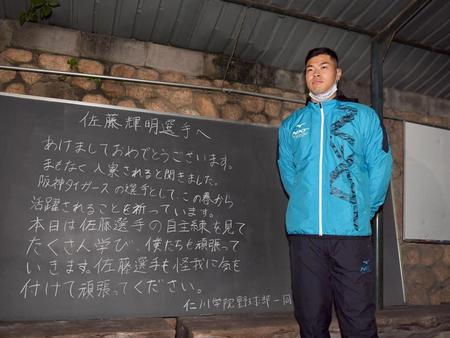 仁川学院野球部の後輩たちが贈ったメッセージの横に立つ佐藤輝（撮影・田中太一）