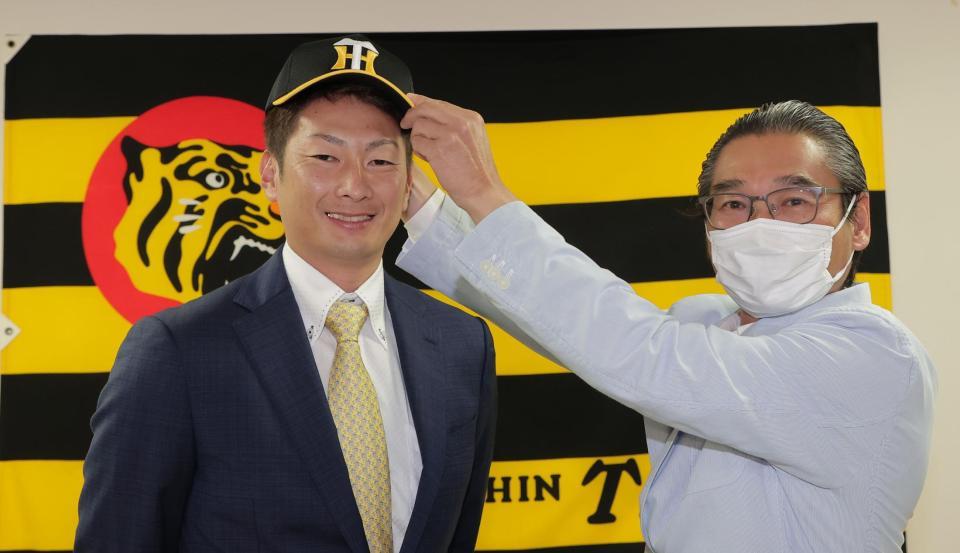 　入団会見で嶌村球団本部長（右）から帽子をかぶせてもらう二保（代表撮影）