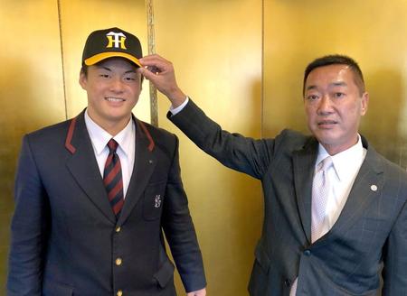 仮契約し、山本スカウト（右）から帽子をかぶせてもらう前川（球団提供）