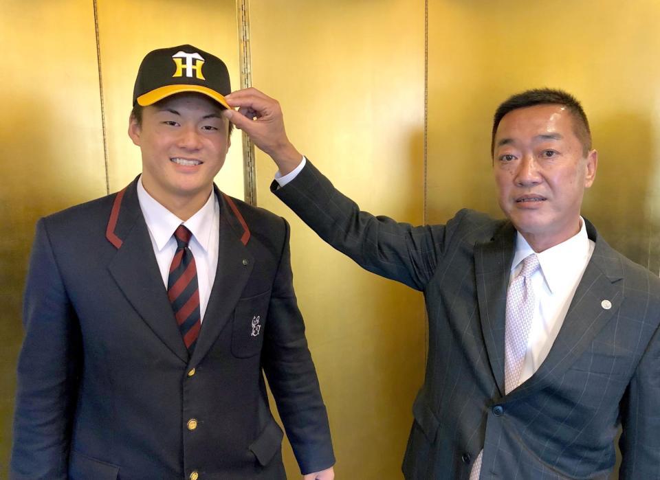 仮契約し、山本スカウト（右）から帽子をかぶせてもらう前川（球団提供）