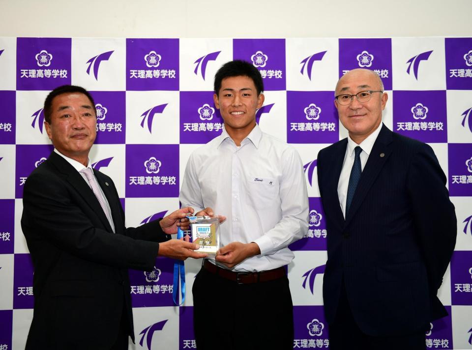 　天理高校・戸井零士は指名あいさつを終え、山本スカウト（左）から岡田監督のサインが入ったドラフト会議のカードを贈られる。（右は畑山統括スカウト）＝撮影・山口登