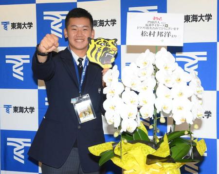 　タレントの松村邦洋から贈られた花の前で岡田監督のサインの入ったＩＤを胸にガッツポーズをする門別（撮影・堀内翔）