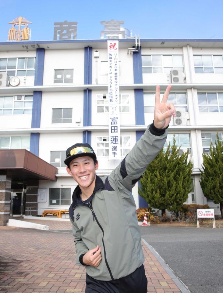 　母校に掲げられた幕の前でポーズを決める富田（撮影・坂部計介）