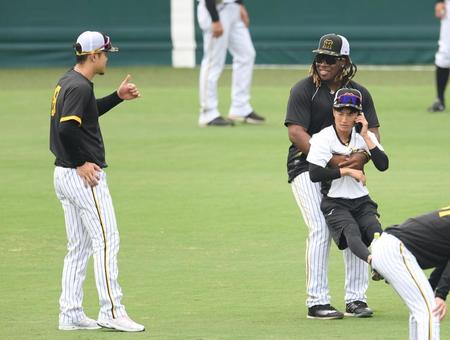 　佐藤輝（左）と話しながら電話中の通訳を抱えるミエセス（撮影・中田匡峻）