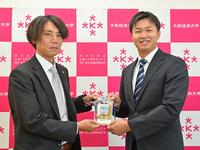 　阪神・渡辺スカウト（左）からドラフト会議で使用したＩＤパスを手渡され笑顔を見せる、大経大・津田淳哉（撮影・立川洋一郎）