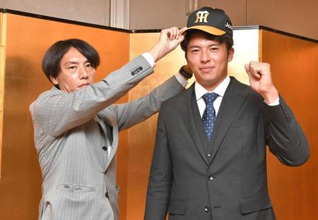 　仮契約を終え、渡辺コーチ（左）から帽子をかぶせてもらう