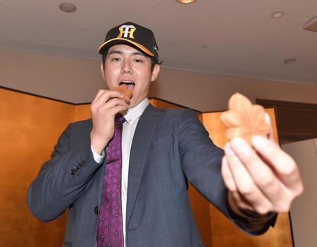 　仮契約を終えた石黒佑弥はもみじ饅頭を手にポーズを決める（撮影・石井剣太郎）