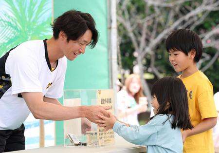 　募金活動に参加した近本光司（左）はこどもと握手を交わす＝１８日