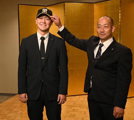 　前田忠節スカウト（右）から帽子をかぶせてもらう阪神ドラフト３位指名の木下里都（撮影・北村雅宏）