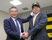 　阪神タイガース入団会見に臨み、嶌村聡球団本部長（左）から帽子をかぶせてもらう楠本（撮影・立川洋一）