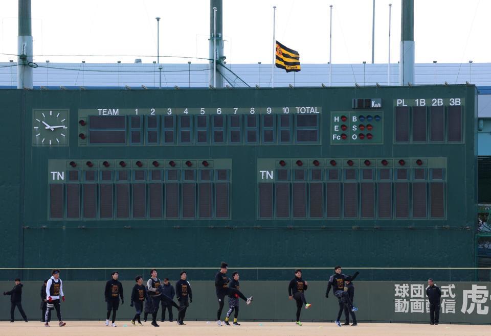 　半旗が掲げられる中、アップをする阪神の新人選手たち（撮影・中田匡峻）