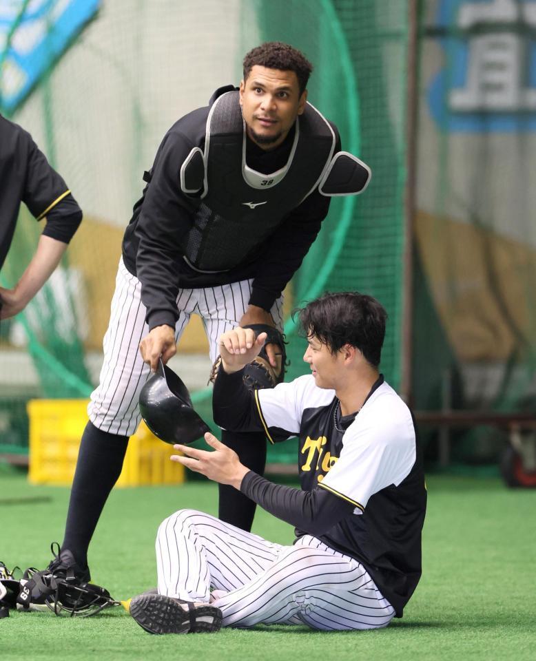 　練習中、栄枝（右）から捕手用防具を受け取るヘルナンデス（撮影・北村雅宏）